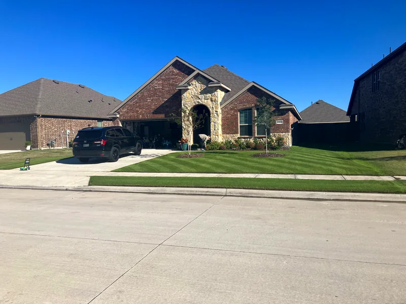 A deep-green, freshly mowed lawn in front of a brick home